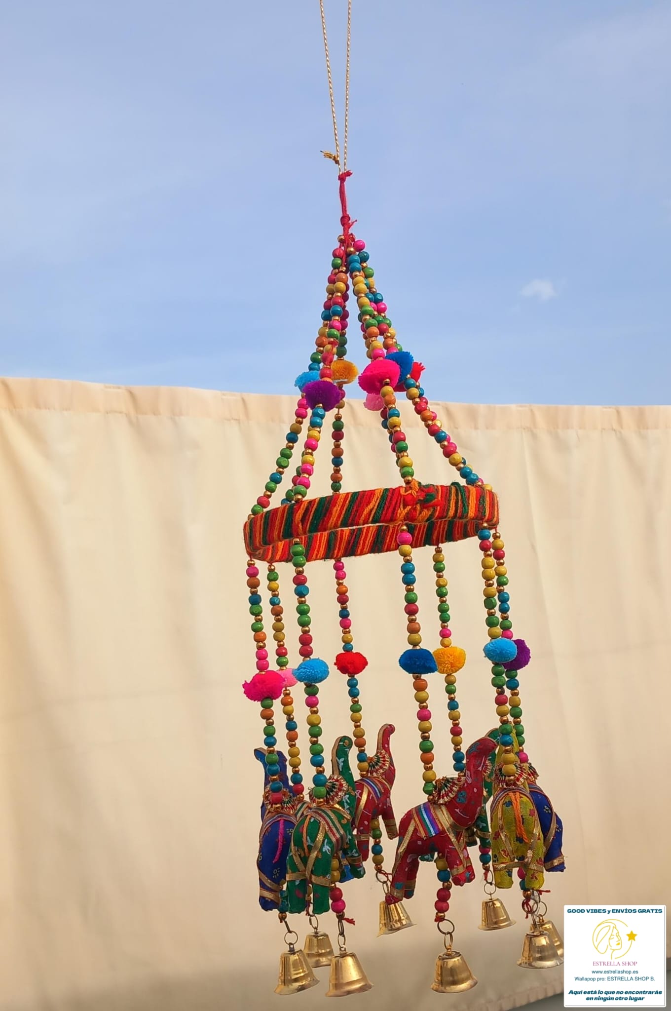 Un colgador encantador que combina tradición y ternura. Este móvil decorativo está elaborado artesanalmente con tela y abalorios,presenta una estructura circular de la que cuelgan ocho elefantes y sus campanas metálicas que producen un suave sonido al moverse con el aire. En su centro,un círculo artesanal entre pompones y cada elefante de la suerte aporta un toque simbólico y alegre. Perfecto para decorar habitaciones infantiles, escaparates o como detalle especial en un rincón de tu hogar. Su estilo suave