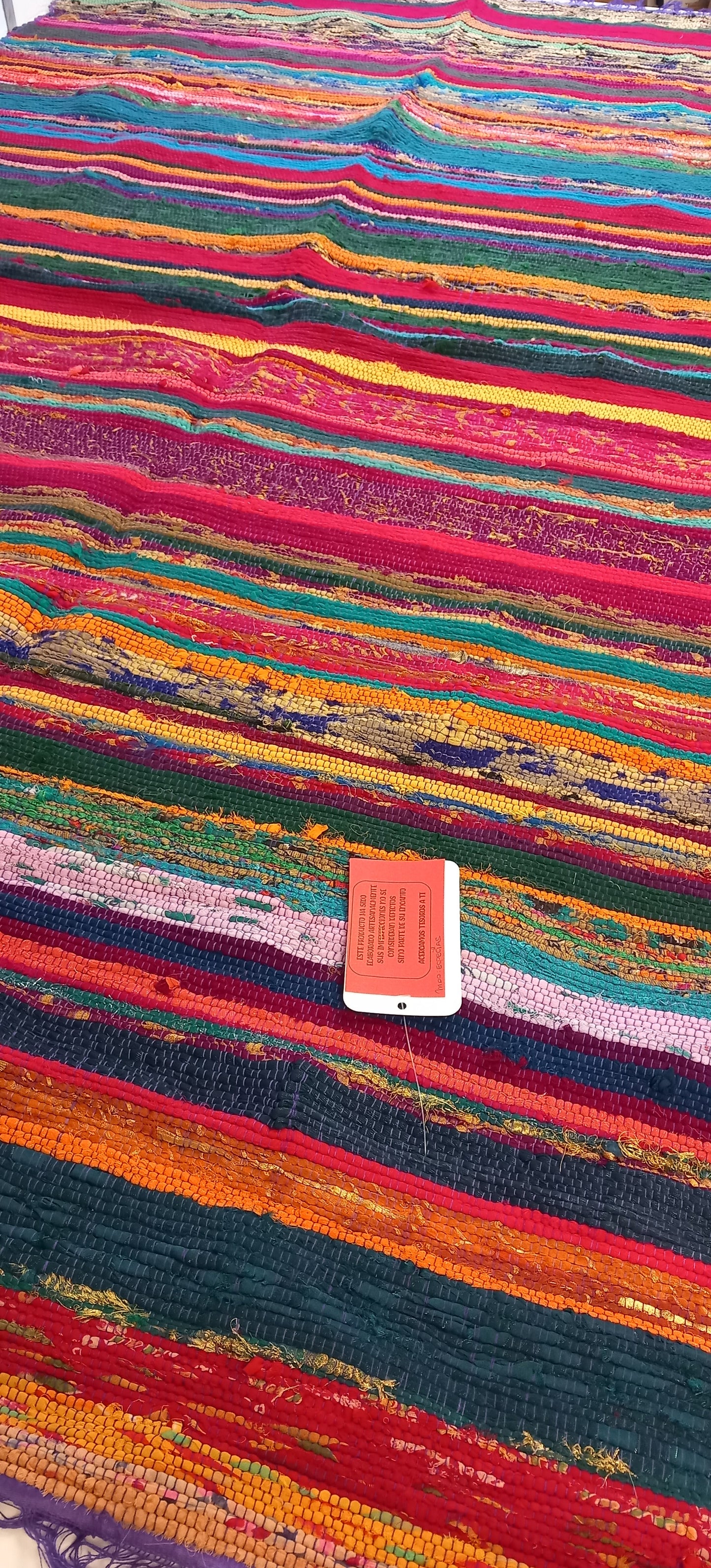 Una explosión de color, textura y tradición en una sola pieza. La jarapa multicolor de 100x200 cm está elaborada artesanalmente con retales de algodón tratados con tintes naturales, lo que da como resultado una alfombra única, vibrante y cargada de carácter. Su diseño mezcla tonos de forma armónica, creando un efecto visual atractivo y cálido. Además de usarse como alfombra, es perfecto como tapiz de pared, cubrecama o para renovar el estilo de muebles y sofás.