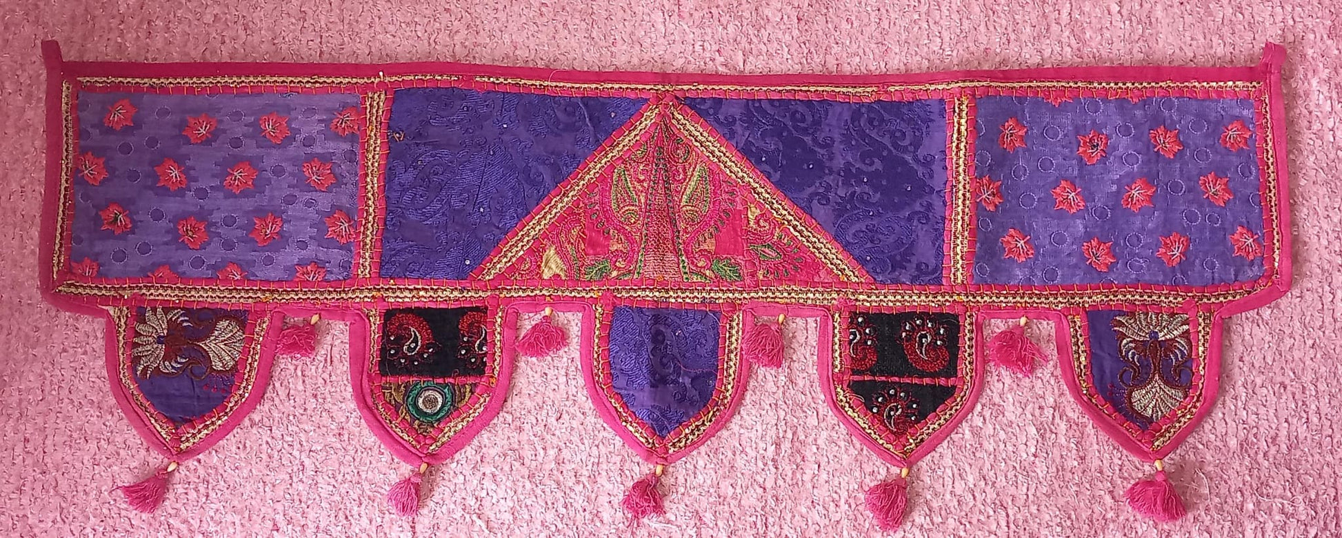 Un toque de tradición y elegancia en cada espacio. El Toran Bordado Patchwork es una pieza artesanal única, confeccionada en algodón con diferentes telas bordadas e hilos metálicos dorados que le aportan un brillo sutil y cómodo. Utilizado en la decoración tradicional hindú para embellecer puertas y atraer buenas energías, su versatilidad permite que también sea perfecto para decorar paredes, muebles, escaparates, mostradores o stands de mercado.