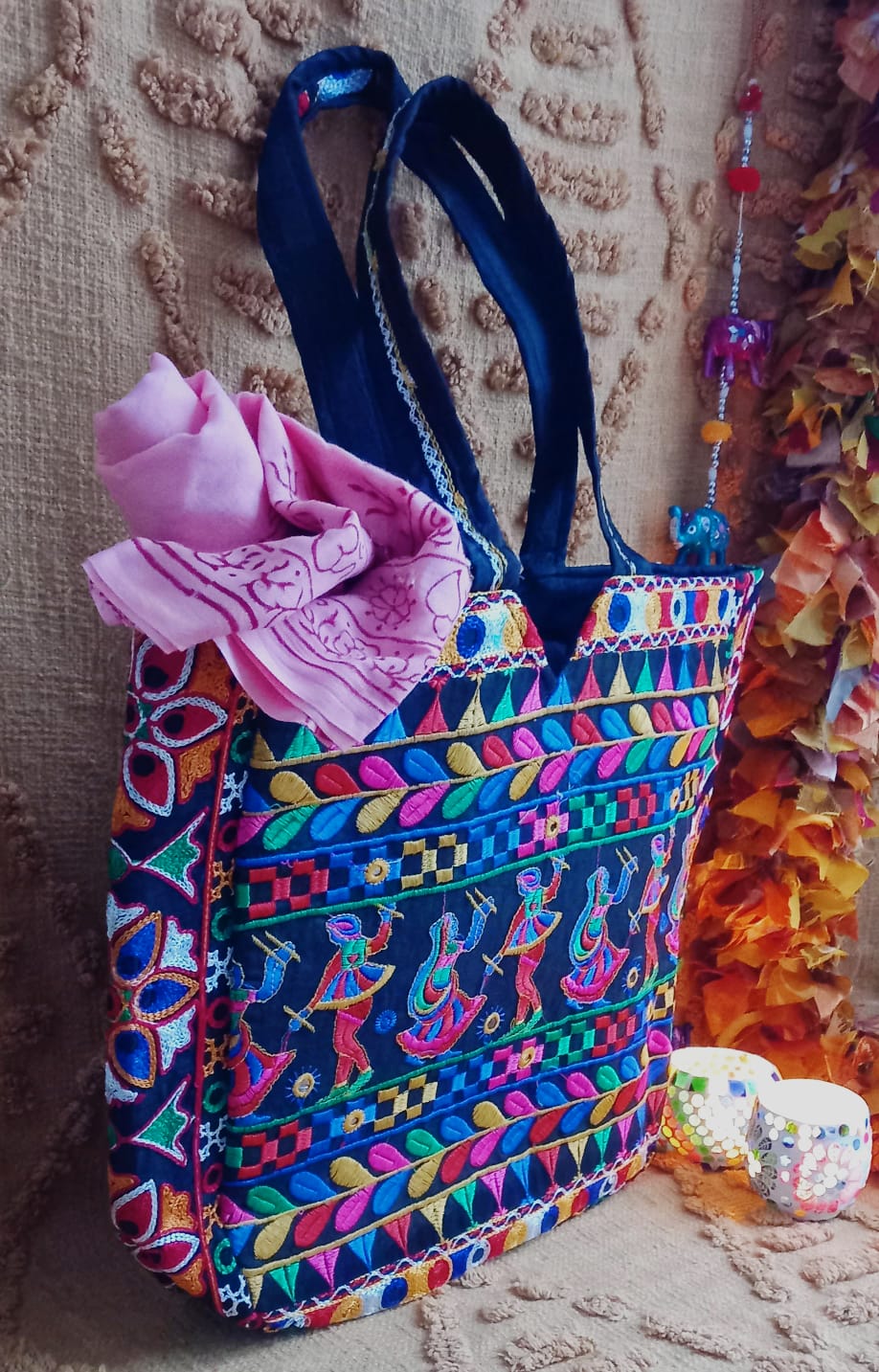 El bolso Frame danza en la india es una pieza original, amplia y con carácter, ideal para ofrecer un toque de exclusividad y color en tu armario. Su diseño tipo capazo destaca por su gran capacidad y su estampado floral bordado con hilos de colores sobre una base negra, creando un contraste vibrante y único. Cuenta con dos asas cómodas para llevar al hombro, cierre de cremallera y varios bolsillos interiores, combinando funcionalidad y estilo. Cada bolso es único, garantizando que adquieres sólo productos a