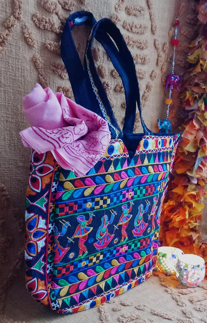 El bolso Frame danza en la india es una pieza original, amplia y con carácter, ideal para ofrecer un toque de exclusividad y color en tu armario. Su diseño tipo capazo destaca por su gran capacidad y su estampado floral bordado con hilos de colores sobre una base negra, creando un contraste vibrante y único. Cuenta con dos asas cómodas para llevar al hombro, cierre de cremallera y varios bolsillos interiores, combinando funcionalidad y estilo. Cada bolso es único, garantizando que adquieres sólo productos a