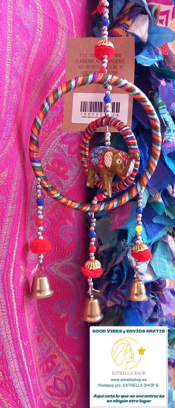 Un colgador encantador que combina tradición y ternura. Este móvil decorativo está elaborado artesanalmente con tela y presenta una estructura circular de la que cuelgan campanas metálicas que producen un suave sonido al moverse con el aire. En su centro, un elefante de la suerte aporta un toque simbólico y alegre. Perfecto para decorar habitaciones infantiles, escaparates o como detalle especial en un rincón de tu hogar. Su estilo suave y colorido lo convierte en un regalo ideal.