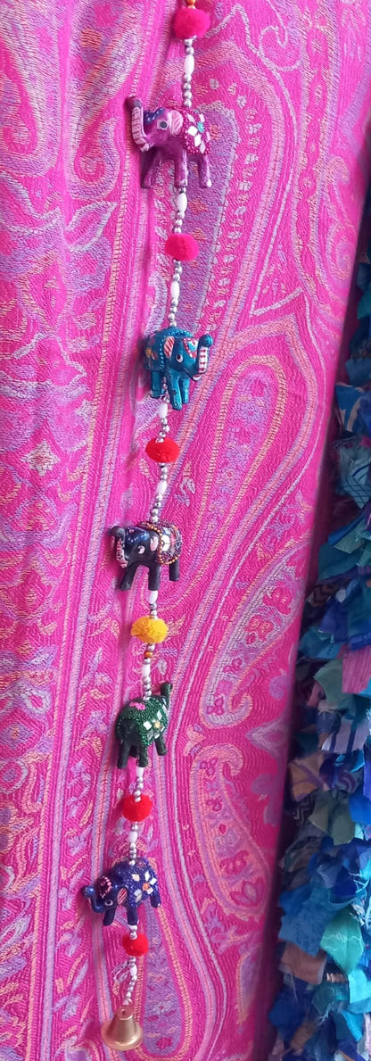 Color, simbolismo y tradición en una sola pieza. Este colgador decorativo con 5 elefantes de la suerte es un accesorio lleno de significado, elaborado artesanalmente con cuentas, pompones, espejos y una pequeña campana al final. Cada elefante, símbolo de sabiduría, fortuna y apertura de caminos en la cultura hindú, aporta un toque alegre y espiritual al ambiente. Ideal para decorar entradas, balcones o espacios interiores, es una pieza vibrante que encantará por su belleza y energía positiva.
 
