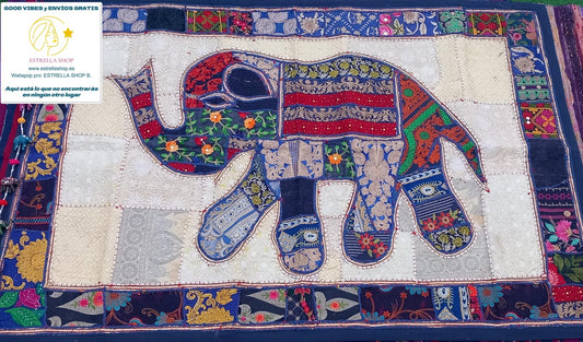 Un clásico del arte textil reinventado con un toque exótico y exclusivo. El tapiz patchwork cuadrado de 150x100 cm está confeccionado artesanalmente con retales bordados en algodón, creando composiciones únicas con flores, formas geométricas y pequeños abalorios brillantes. Cada pieza tiene su propio carácter, con un ribete en tono coordinado que enmarca el diseño y lo convierte en una joya decorativa. Ideal para colgar, usar como camino de mesa o sobre un mueble que quieras destacar.